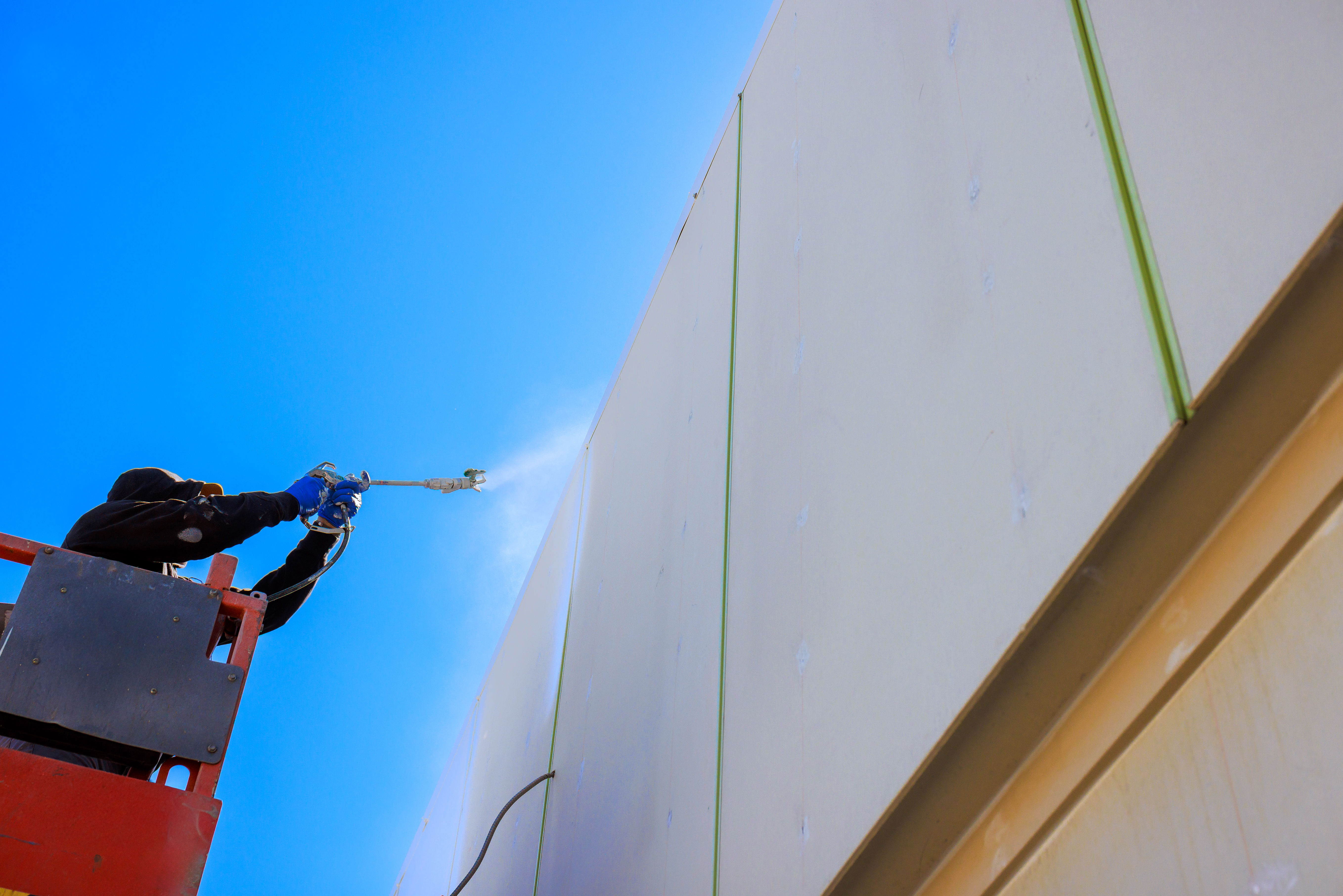 Painter applies paint to building wall from high lift on works day